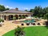 Expansive stone patio featuring a freeform swimming pool with integrated spa, a covered loggia with stone pillar accents, and a manicured lawn