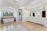 Freestanding soaking tub, walk-in shower with marble-finish walls, dual vanity with extensive storage, full-height wall mirror, and chandelier lightin