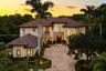 Stucco exterior featuring a tile roof, stone masonry accents, arched window detailing, and a paved motor court