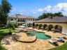 Expansive backyard featuring a custom free-form pool, integrated spa, sprawling stone-paved patio, and a covered loggia with stone-finished pillars