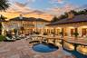 Mediterranean-inspired estate featuring a sprawling stone-paver pool deck, a freeform swimming pool, a covered lanai with arched architectural detaili