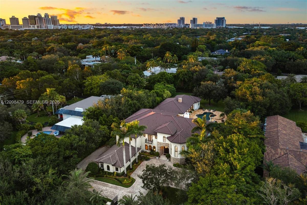 Aerial view of a multi-level estate featuring a tile roof, light-toned masonry exterior, paver driveway, and a backyard swimming pool
