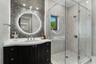 Vanity with integrated sink and chrome fixtures, illuminated round mirror, geometric wall tile, glass-enclosed shower, and herringbone tile shower sur