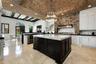 Exposed brick vaulted ceiling with recessed lighting, large central kitchen island with light-colored countertop, white cabinetry, dark stone countert