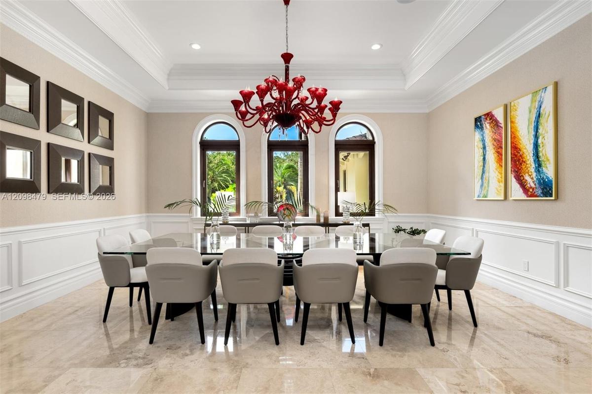 Recessed ceiling with layered crown molding, arched windows, wainscoting, and large format tile flooring