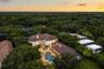 Aerial perspective of an expansive residence featuring a multi-gabled tile roof, stone-paved pool deck, custom-shaped swimming pool with integrated sp
