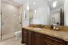 Frameless glass shower enclosure with tiled walls, wood-finish vanity with stone countertop, and two pendant light fixtures