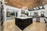 Vaulted brick ceiling, large central island with light-toned countertop, stainless steel appliances, dark wood island cabinetry, and light-toned floor