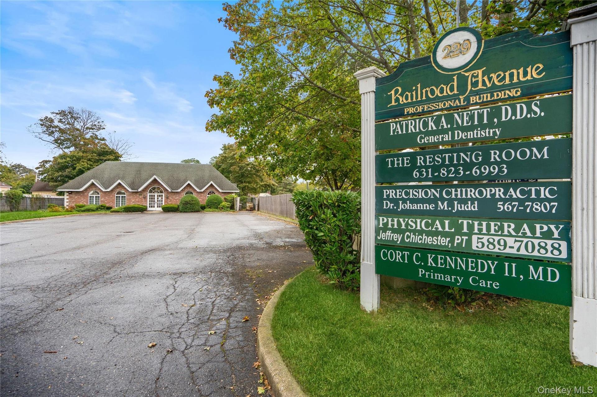Professional building featuring brick exterior construction, multi-gabled roofline, asphalt parking area, and dedicated roadside signage
