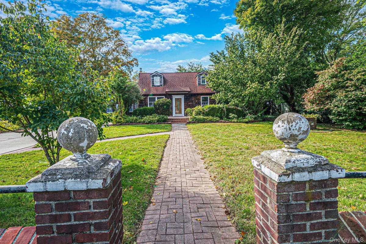 Cape Cod exterior featuring shingle siding, a brick walkway, and twin brick entrance pillars topped with spherical finials
