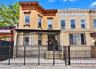 Multi-story masonry facade featuring detailed cornice work, a structural bay, metal window security bars, and a metal perimeter fence