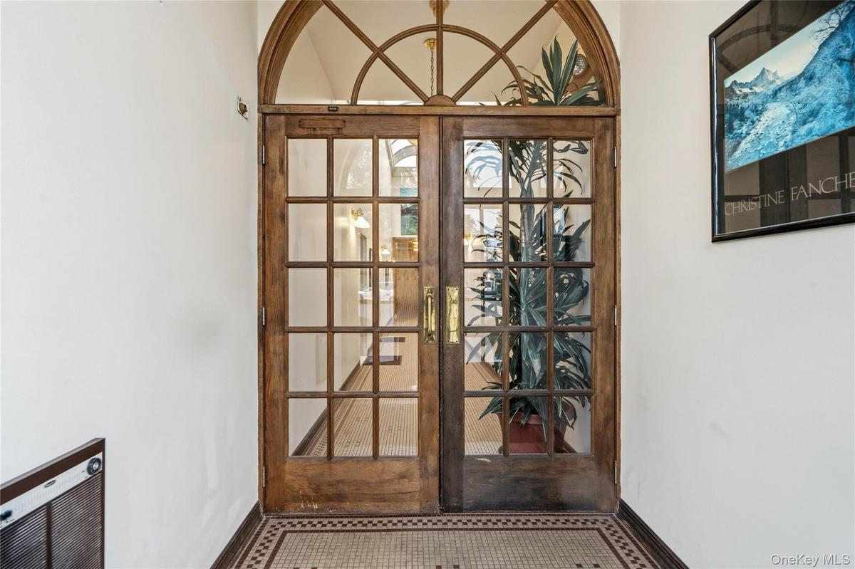 Double wood-framed glass entry doors featuring a decorative arched transom, multi-pane glazing, and brass hardware, accented by tiled flooring with a 
