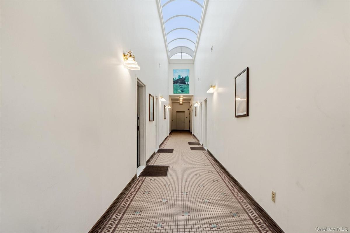 Hallway featuring an arched vaulted skylight, patterned tile flooring, and wall-mounted sconce lighting