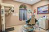 Treatment room featuring a dental chair, digital radiography unit, multi-drawer cabinetry, and a decorative arched window with a stained-glass transom