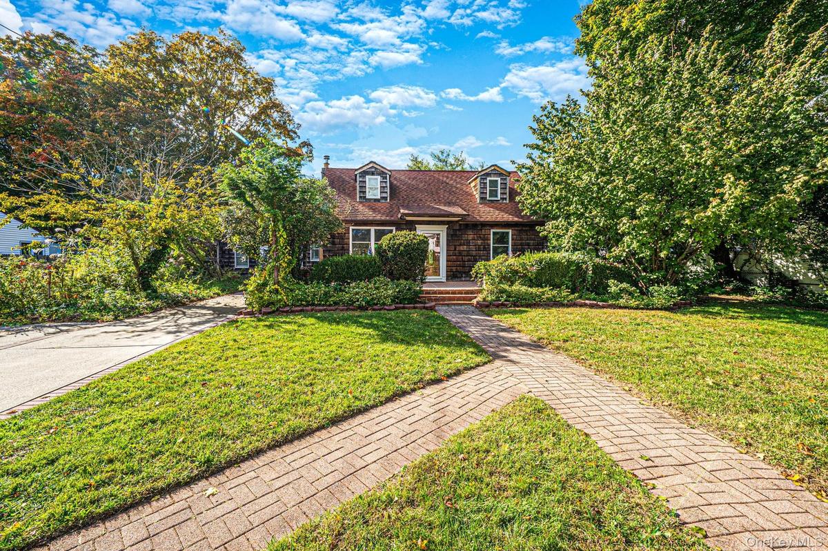 Cape Cod style residence featuring wood-shingle siding, dual doggie dormer windows, a brick front stoop, and a herringbone-patterned brick walkway