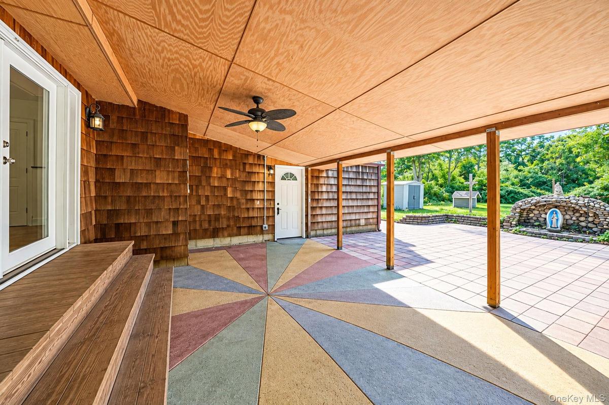Covered outdoor patio featuring shingle siding, wood-paneled ceiling, ceiling fan, and decorative geometric concrete flooring