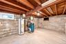 Utility area featuring exposed wood ceiling joists, concrete block walls, concrete flooring, water heater, and boiler system