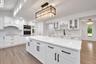 Kitchen featuring a large central island with light-toned stone surfacing, white cabinetry with matte black hardware, integrated wine rack, and a line