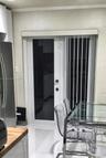 Full-light glass exterior door featuring a white frame and brushed metal hardware, complemented by white vertical blinds and neutral textured wall fin