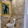 Full-height stone wall tiling, porcelain commode, and stainless steel grab bars