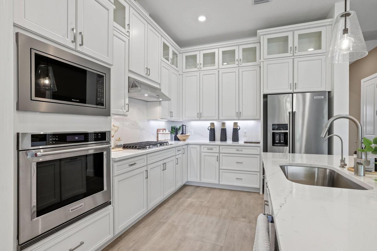 Kitchen featuring white shaker-style cabinetry with glass-front uppers, stainless steel appliances, stone countertops, and wood-finish flooring