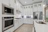 Kitchen featuring white shaker-style cabinetry with glass-front uppers, stainless steel appliances, stone countertops, and wood-finish flooring