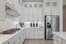 White shaker-style cabinetry with glass-front uppers, light-toned stone-finish countertops, full-height stone-finish backsplash, stainless steel gas c