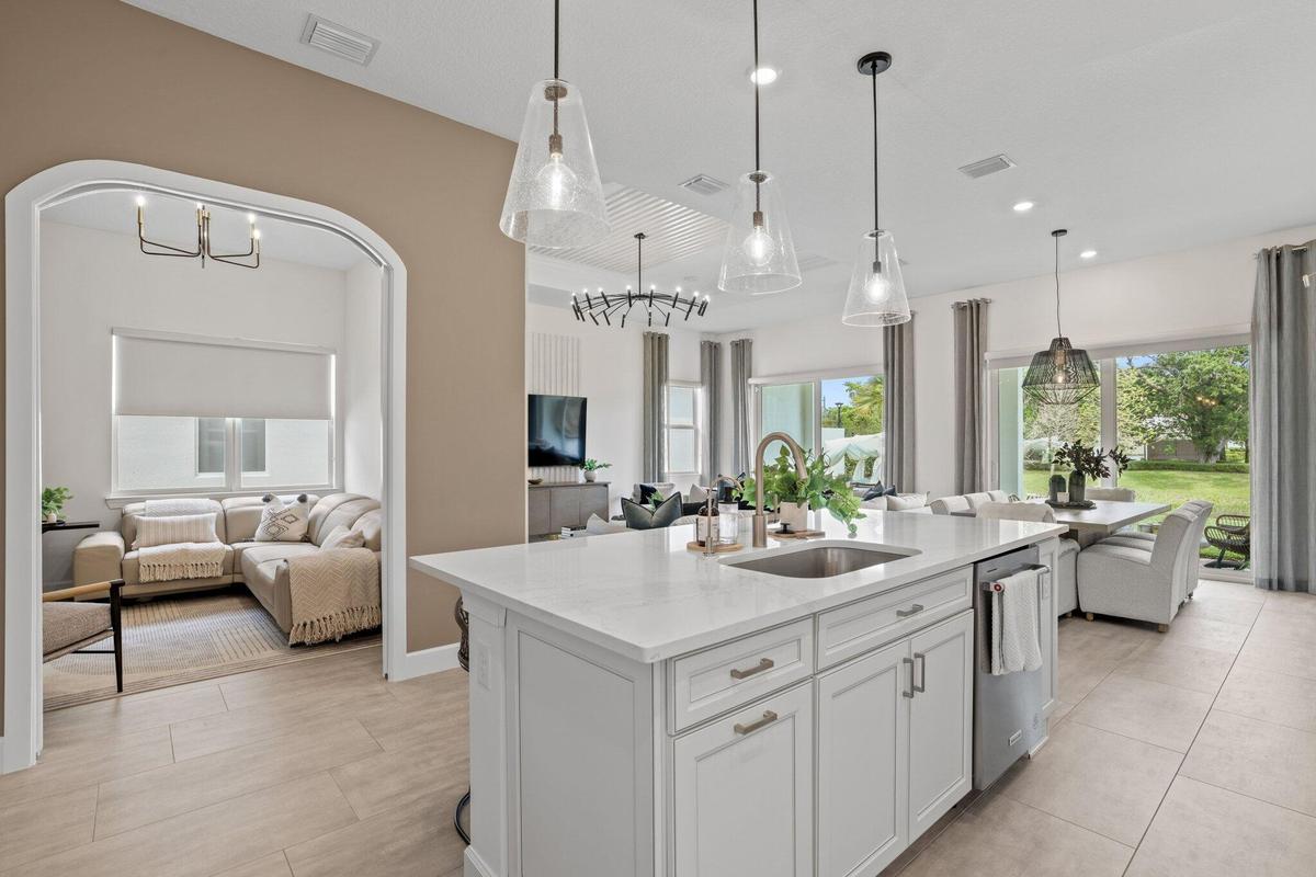 Kitchen featuring a center island with quartz countertops, custom shaker-style cabinetry, stainless steel sink, and glass pendant lighting, complement