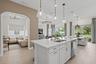 Kitchen featuring a center island with quartz countertops, custom shaker-style cabinetry, stainless steel sink, and glass pendant lighting, complement