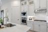 Kitchen featuring white cabinetry, quartz countertops with a full-height stone backsplash, stainless steel built-in double ovens, a gas cooktop, and a
