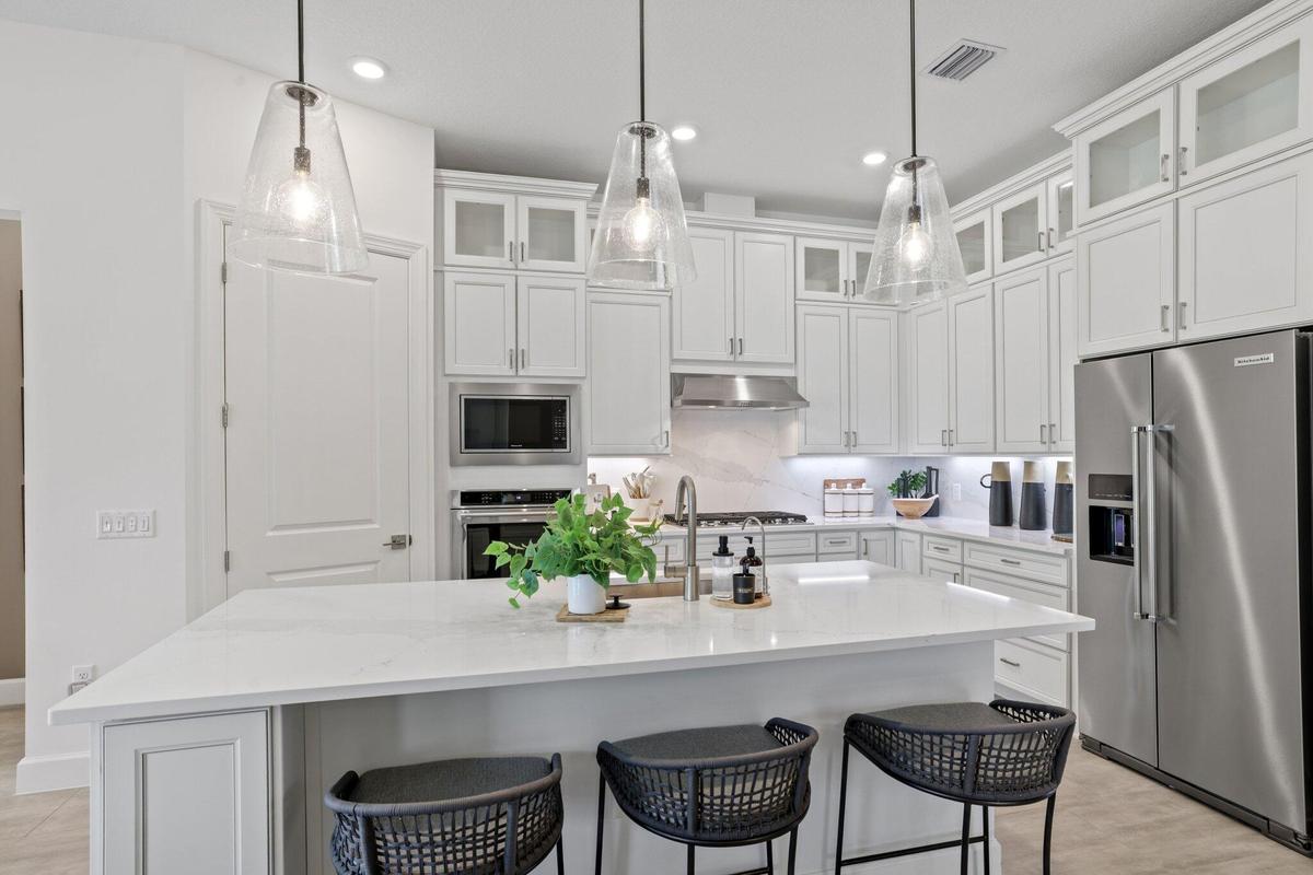 Kitchen featuring white cabinetry with glass-front uppers, solid-surface countertops, a large center island, stainless steel appliances, and three cle