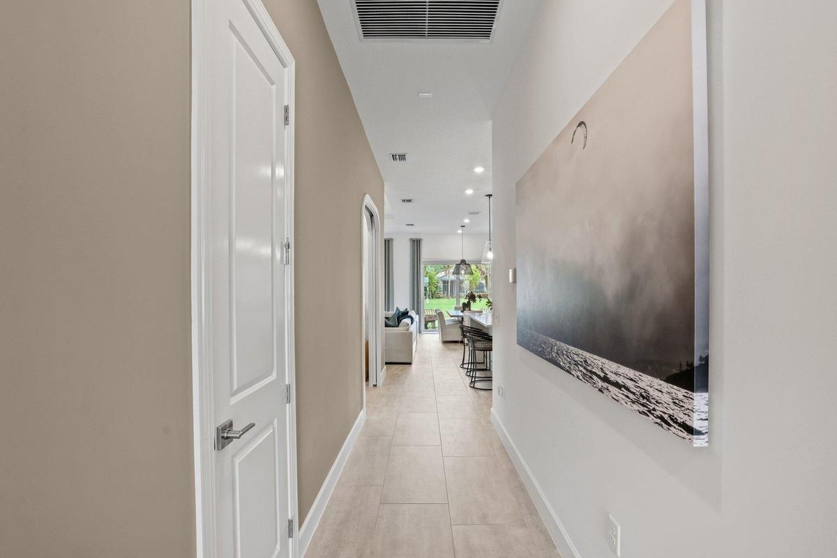 Interior hallway featuring large-format ceramic tile flooring, neutral wall paint, a multi-panel door with metallic hardware, and recessed lighting