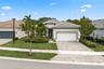 Stucco exterior featuring a tiled roof, paver driveway, two-car garage, and manicured landscaping