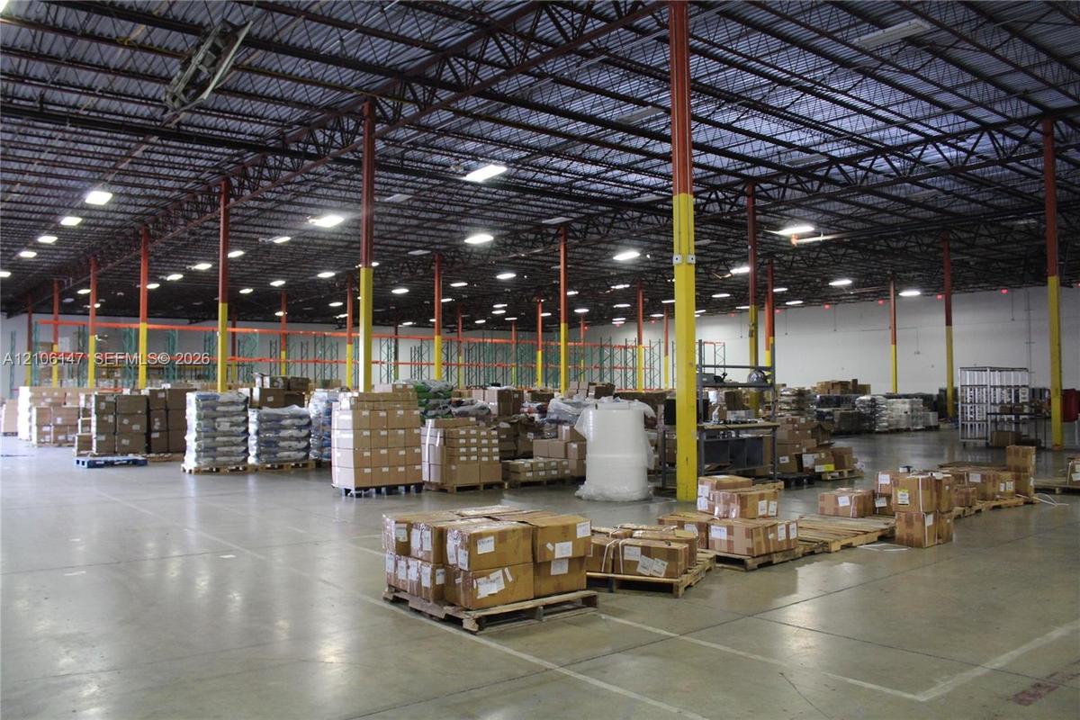 Industrial warehouse facility featuring high-clearance exposed steel truss ceilings, polished concrete flooring, extensive overhead LED lighting, and 