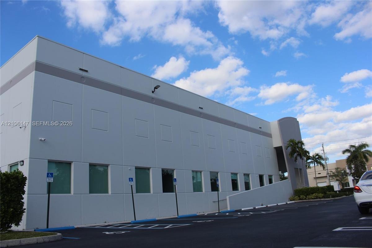 Multi-story concrete exterior with a smooth finish, exterior security cameras, designated parking spaces, and concrete ramp access