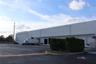 Industrial facility exterior featuring multiple loading docks, an expansive asphalt-paved lot, and white precast concrete panels