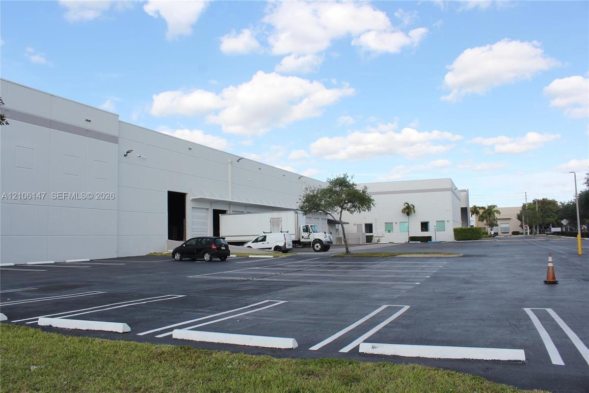 Industrial structure featuring concrete tilt-wall construction, multiple loading docks, and an expansive asphalt parking lot with marked stalls