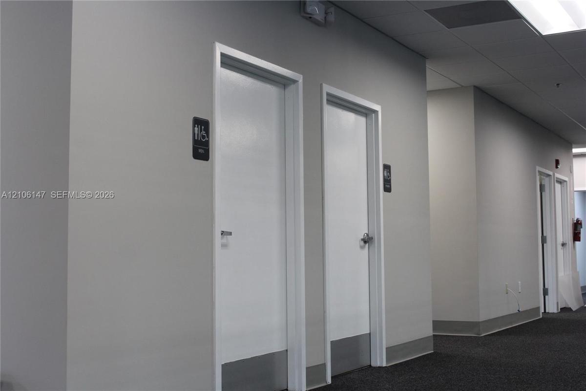 Commercial hallway featuring neutral-toned walls, recessed ceiling lighting, carpeting, and multiple interior doors with metal kick plates