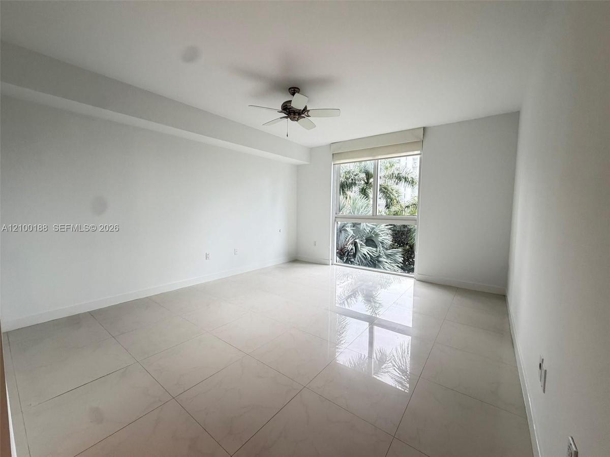 Neutral-toned room featuring large-format tile flooring, a ceiling fan, and a multi-pane window with exterior greenery
