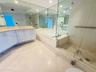 Bathroom featuring a double vanity with light-toned countertop, soaking tub with tile surround, glass-enclosed shower, expansive wall-to-wall mirrors,