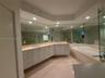 Dual vanity featuring light-toned cabinetry, a neutral countertop, recessed lighting, expansive wall mirrors, and an integrated soaking tub