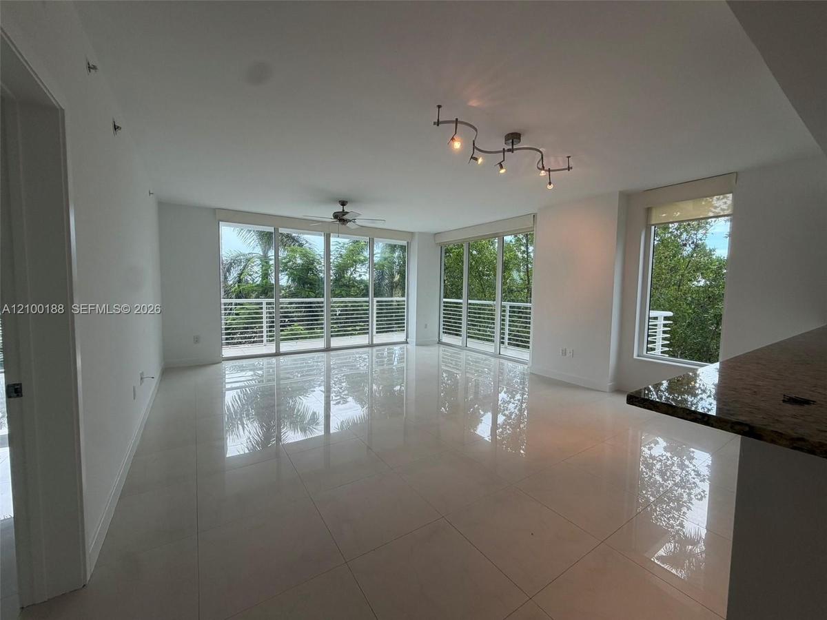 Open-concept interior featuring large-format tile flooring, expansive floor-to-ceiling windows, track lighting, a ceiling fan, and a stone-surface bre
