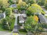 Shingle-sided residence with a dark-pitched roof, paved driveway, stone walkway, and established landscaping