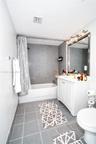 Bathroom featuring a white vanity cabinet, a rectangular mirror with a metal frame, a multi-bulb vanity light fixture, and a bathtub with gray tile su