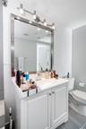 White vanity featuring a smooth countertop with an integrated basin, polished metal hardware, a large framed mirror, and four-light vanity fixture