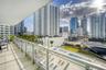 Covered balcony featuring tile flooring and a glass-paneled railing overlooking an urban skyline and multi-level swimming pools