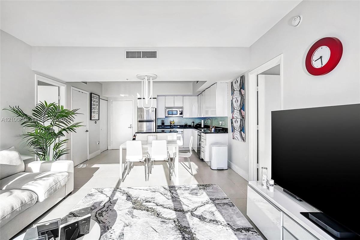 Open-concept kitchen featuring high-gloss cabinetry, stone countertops, stainless steel appliances, and a central peninsula