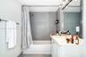 Bathroom featuring a white vanity with a rectangular sink, wall-to-wall mirror, chrome light fixture, and a shower-tub combination with large-format g