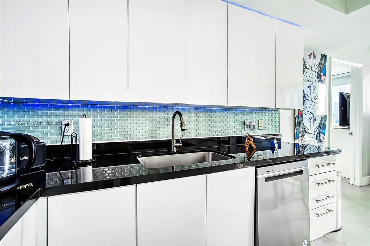 Kitchen featuring flat-panel white cabinetry, black stone countertops, an undermount stainless steel sink, a stainless steel dishwasher, and a glass t