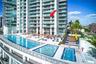 High-rise condominium building featuring glass exterior wall panels and private balconies, complete with a multi-tier swimming pool deck, integrated w